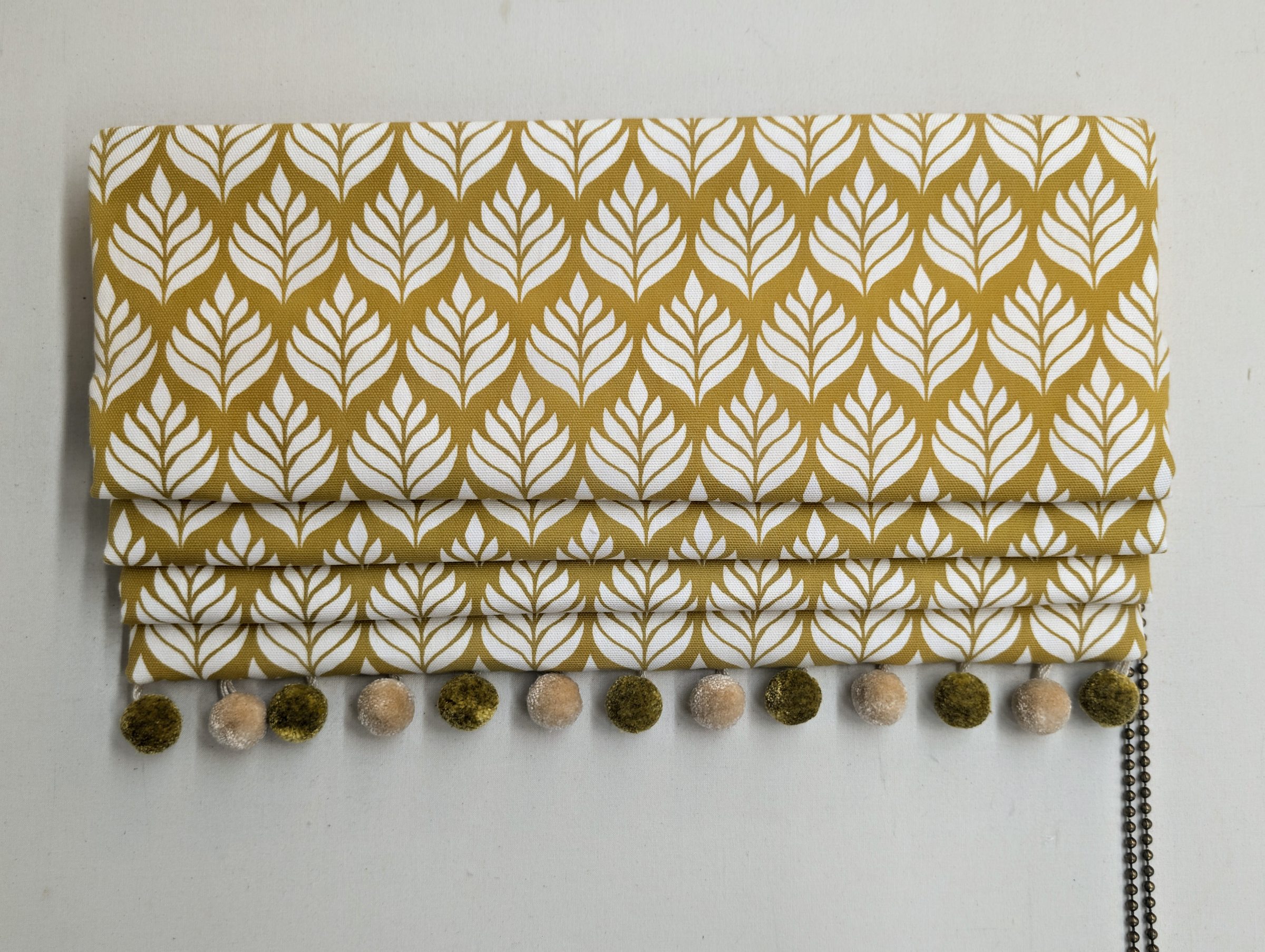 Roman blind in a leaf-print fabric, finished with a hand-made pom-pom trim