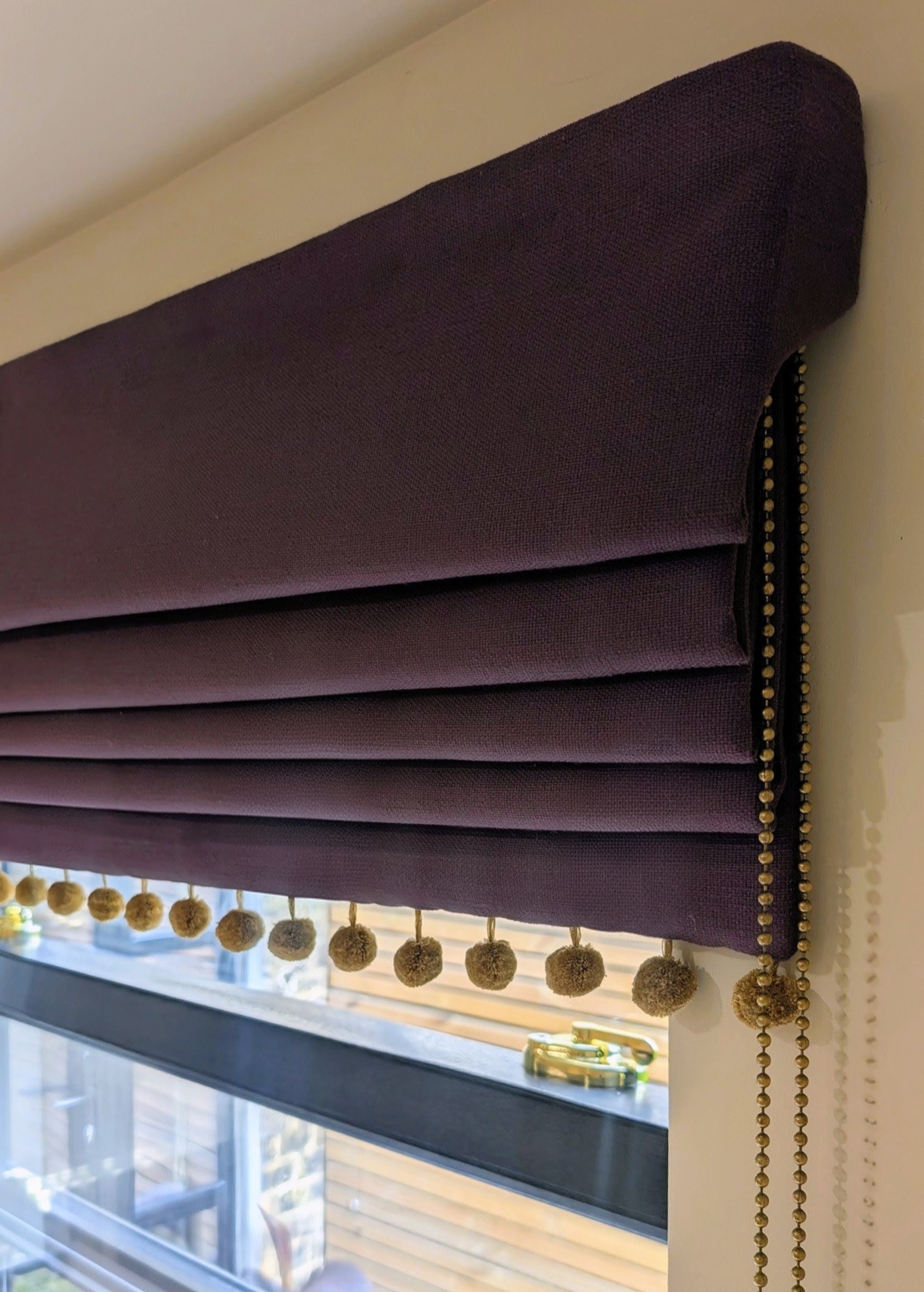 Aubergine cascade Roman blind with a gold pom-pom trim and a deep side return