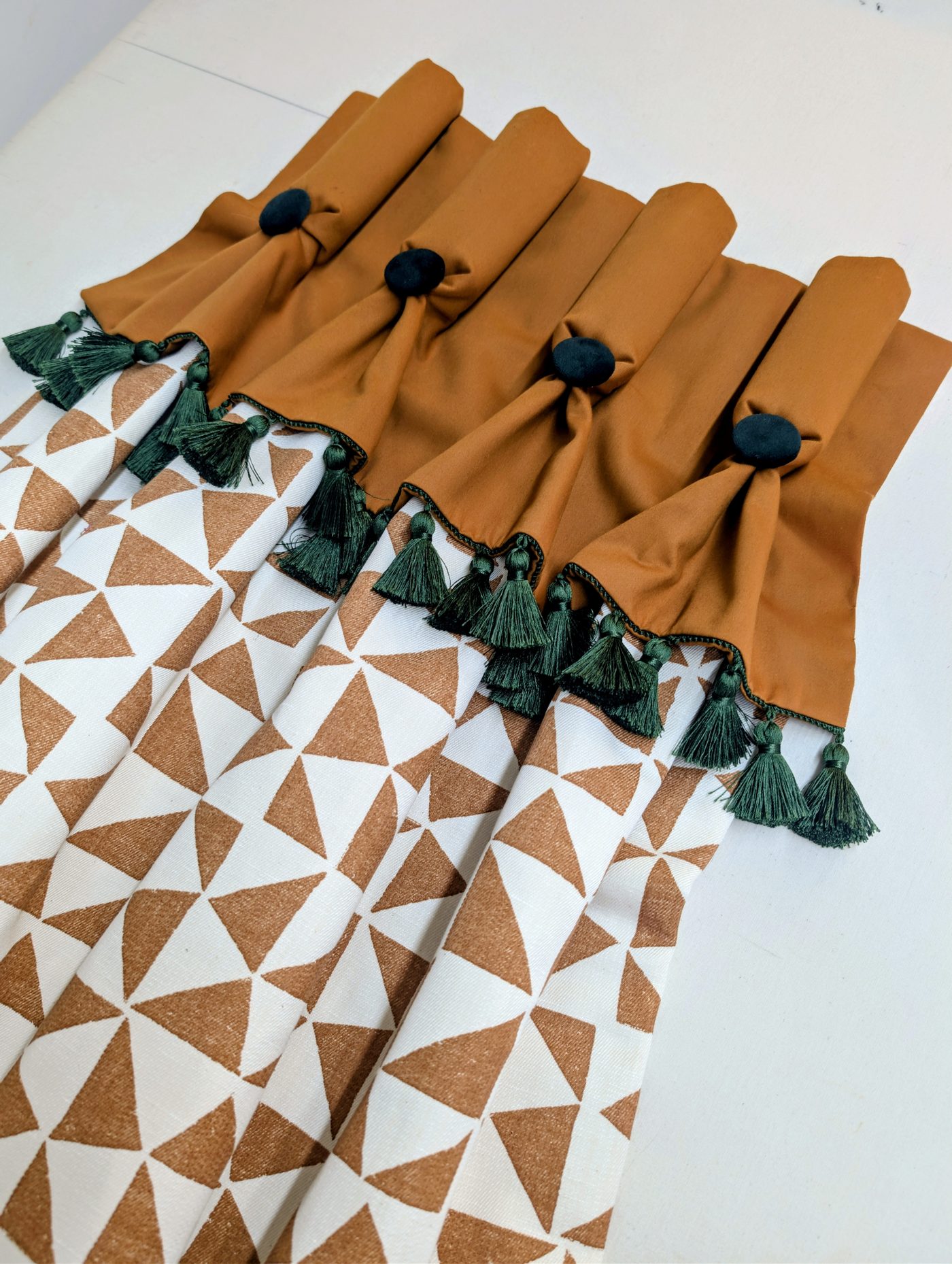 Ochre pelmet finished with dark green tassels, laid over a geometric print fabric
