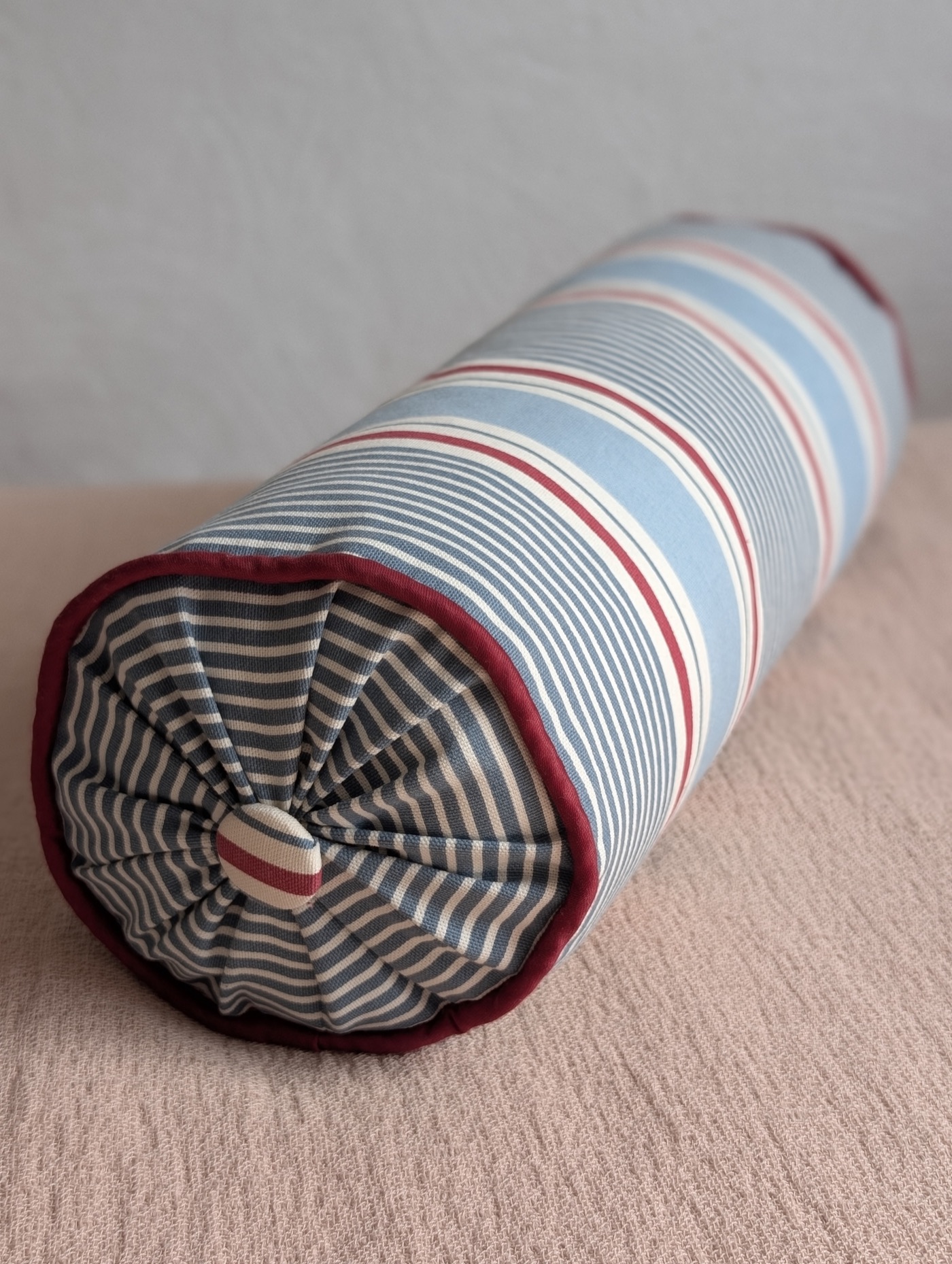 Striped bolster cushion with contrast red piping and a gathered, button-finished end